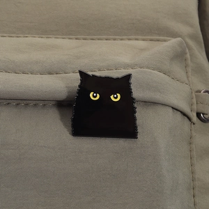 Détail du pin's chat noir avec yeux jaunes attaché à un sac à dos en toile kaki résistant