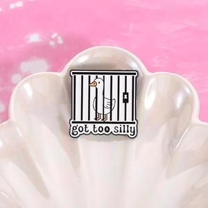 Close-up of funny enamel goose pin in cage with got too silly text on shell tray