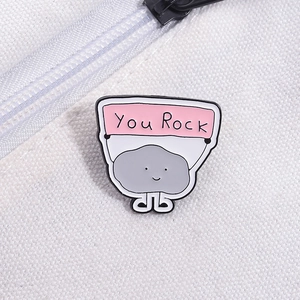 Detail of a cartoon stone enamel pin with You Rock banner on a canvas bag strap