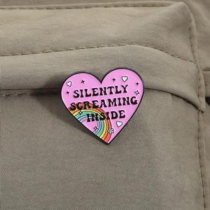 Heart-shaped enamel pin with rainbow and Silently Screaming Inside text on a backpack
