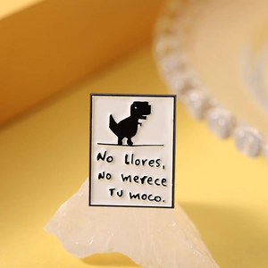 Macro shot of white enamel pin with dinosaur and Spanish quote on crystal stone