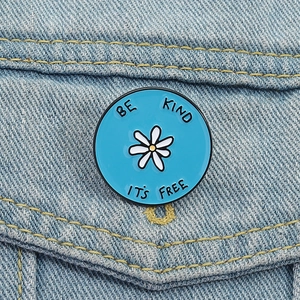 Makroaufnahme der blauen Emaille-Gänseblümchen-Brosche an Jeansjacke mit Be Kind It's Free