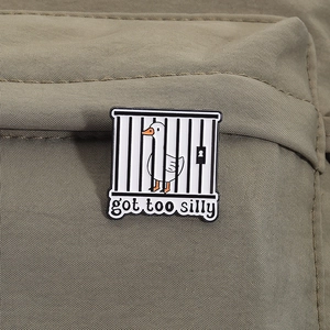 Detail of funny enamel pin featuring a white goose in a cage with got too silly text