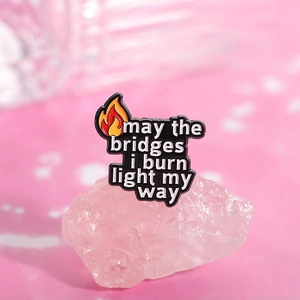 Detailed macro view of motivational enamel pin on pink crystal stone with flame quote