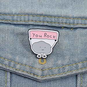 Detail of cute You Rock stone enamel pin pinned on a denim jacket pocket edge