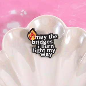 Enamel flame badge brooch with 'may the bridges i burn light my way' on shell tray