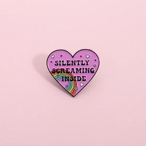 Rainbow heart enamel pin with Silently Screaming Inside text on pink background