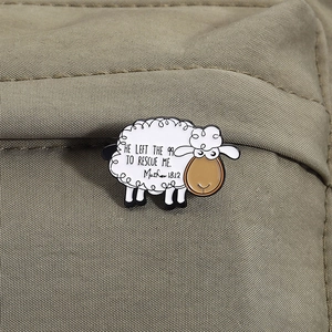 Detalle de pin esmaltado de oveja blanca con versículo bíblico sobre tela verde