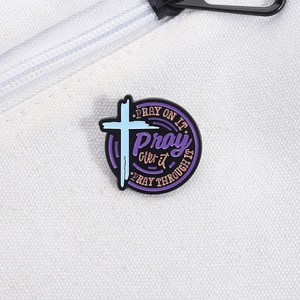 Detail of round religious enamel pin with purple lettering and cross on a canvas bag