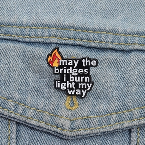 Detail of inspirational quote enamel pin on denim jacket featuring burning bridge design