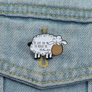 Detalle de pin esmaltado de oveja con cita religiosa sobre tejido vaquero azul