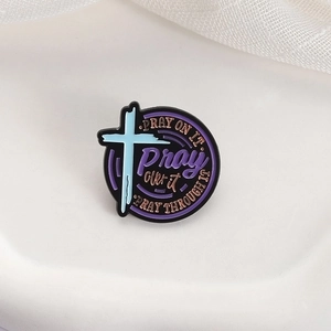 Religious enamel pin with cross and pray on it quotes on white fabric background