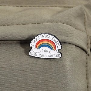 Detail of a rainbow and cloud enamel pin with witty quote on green fabric background