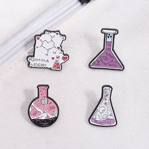 Close-up of laboratory beaker enamel pins with scientific motifs on white canvas bag