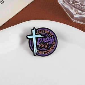 Round enamel prayer pin with cross and 'Pray on it' quote on a ceramic plate