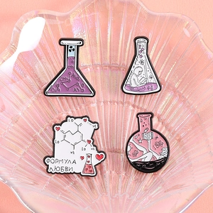 Set of four chemistry enamel pins with beakers and love formula on a shell tray