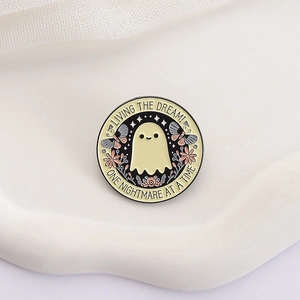 Detalle de pin esmaltado de fantasma con flores y texto sobre un soporte blanco de gala