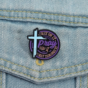 Detail of round religious enamel cross pin attached to a light blue denim jacket pocket
