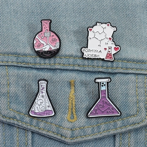 Detail of four creative enamel pins on denim featuring lab flasks and chemistry formulas