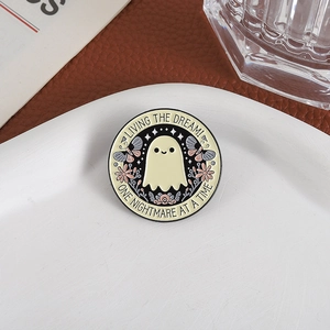 Detalle del pin esmaltado redondo con fantasma, flores y texto sobre cerámica blanca