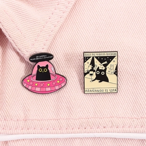 Détail de broches en émail représentant un ovni et un chat noir sur du denim rose