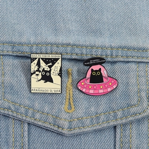 Détail de pins en émail chat noir épinglés sur du tissu denim bleu clair avec texte espagnol