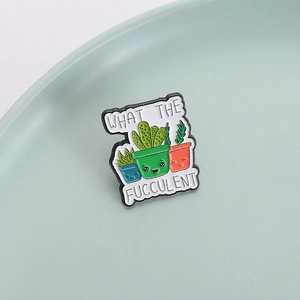 Funny cartoon cactus enamel pin with WHAT THE FUCCULENT pun on a ceramic tray