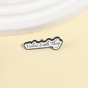 Broche en émail avec texte 'Violent Little Thing' noir et blanc sur fond beige neutre