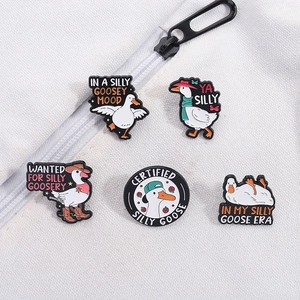 Detailed close-up of five enamel goose pins with funny quotes on textured fabric