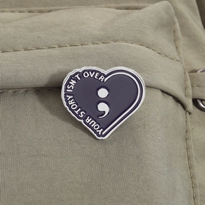 Inspirational heart enamel pin with semicolon and Your Story Isnt Over quote on a bag