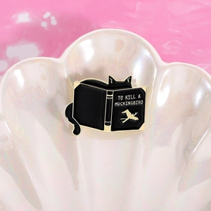 Macro detail of To Kill a Mockingbird black cat enamel pin on iridescent shell bowl