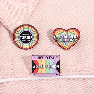 Detailed view of three rainbow enamel pins with LGBTQ+ inclusive quotes on pink denim