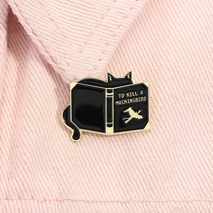 Detail of a black cat reading a book enamel pin on pink denim fabric background