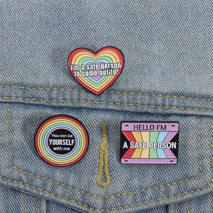 Close-up of three rainbow enamel pins on a denim jacket showing LGBTQ+ support