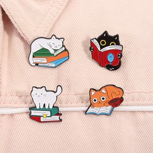 Set of four colorful enamel cat pins showing cats with books on pink denim fabric