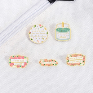 Detail of five enamel pins with floral, candle designs and inspirational quotes on fabric
