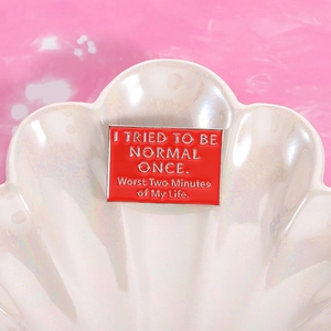 Rode emaille pin met humoristische quote op roze schelpachtergrond voor kleding en tassen