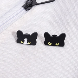Detail of two cute black cat enamel pins with yellow eyes on a white canvas backpack