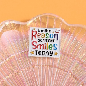 Macro di una spilla quadrata smaltata con citazione positiva su un vassoio a conchiglia