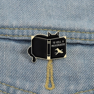 Detail shot of a black cat enamel pin on denim showing To Kill A Mockingbird design