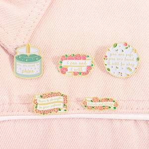 Detail view of five enamel pins with floral and candle designs on pink fabric background