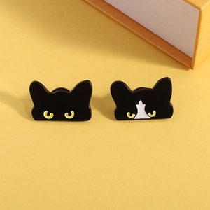 Close-up of black and tuxedo cat enamel pins with yellow eyes on a yellow background