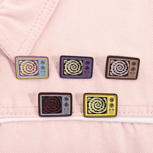 Set of five colorful retro TV enamel pins showcased on pink denim fabric texture