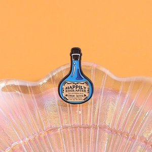 Detail of blue potion enamel pin with True Love text on an iridescent shell base