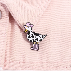 Detailed close-up of a cartoon cow-patterned duck enamel pin on a denim collar