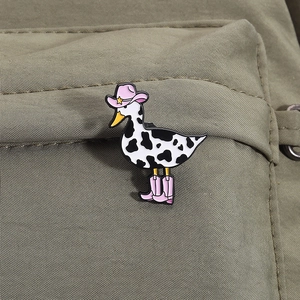 Detailed view of an enamel duck brooch with cow print and pink cowboy boots on canvas