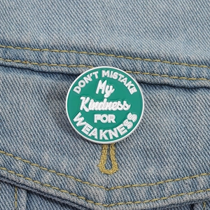 Dettaglio della spilla smaltata verde tonda con citazione bianca su denim blu