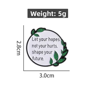 Detail view of round white enamel pin with inspirational quote and green leaf accents