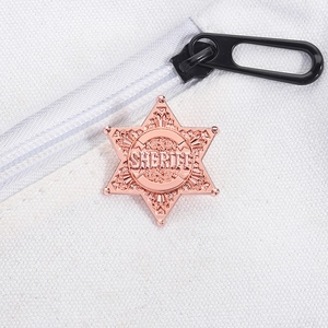 Macro detail of a rose gold sheriff badge pin on white canvas next to a zipper