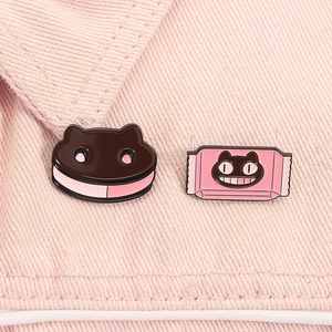 Detail of pink cat biscuit and candy enamel pins pinned on pink denim fabric material